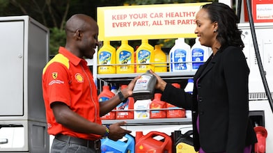 A red Ferrari sitting on a Shell station forecourt with a man leaning on a petrol pump